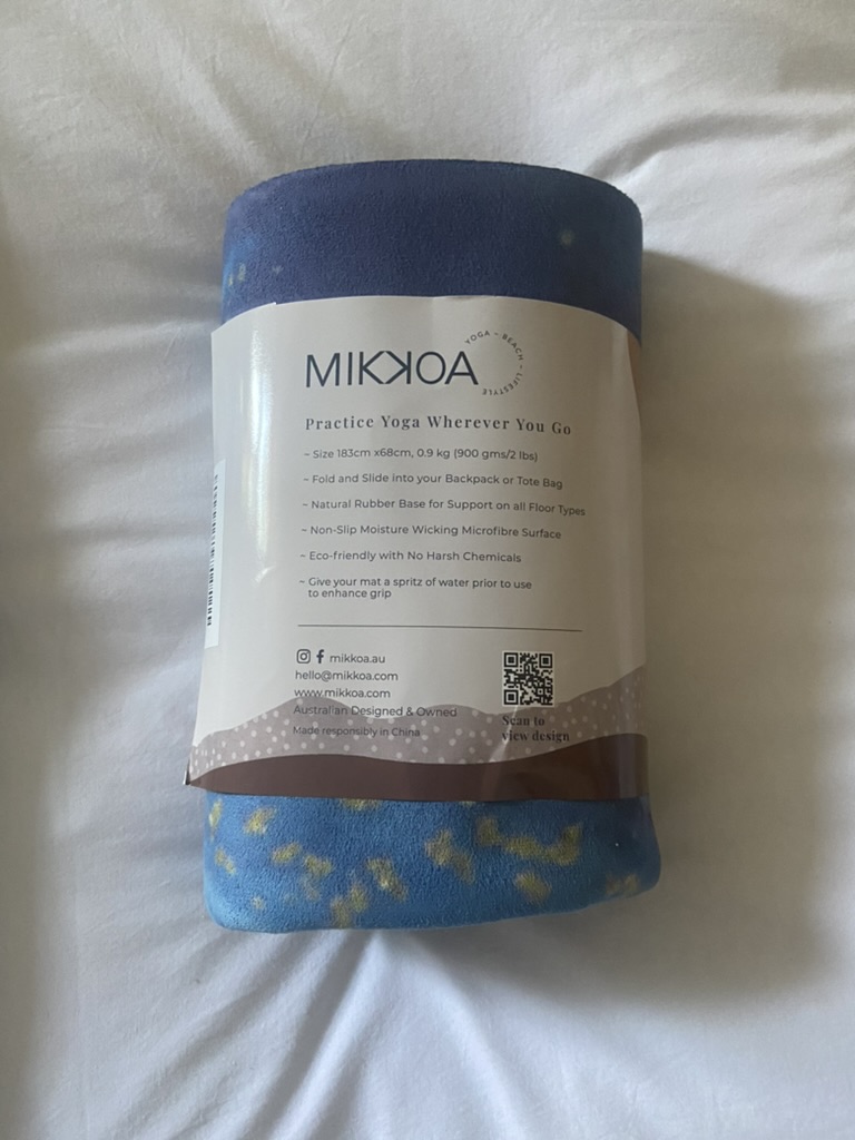 Mi reseña de la esterilla de yoga de viaje Mikkoa – Esterilla plegable para viajar Esterilla de yoga de viaje Mikkoa enrollada con su etiqueta de características sobre una cama