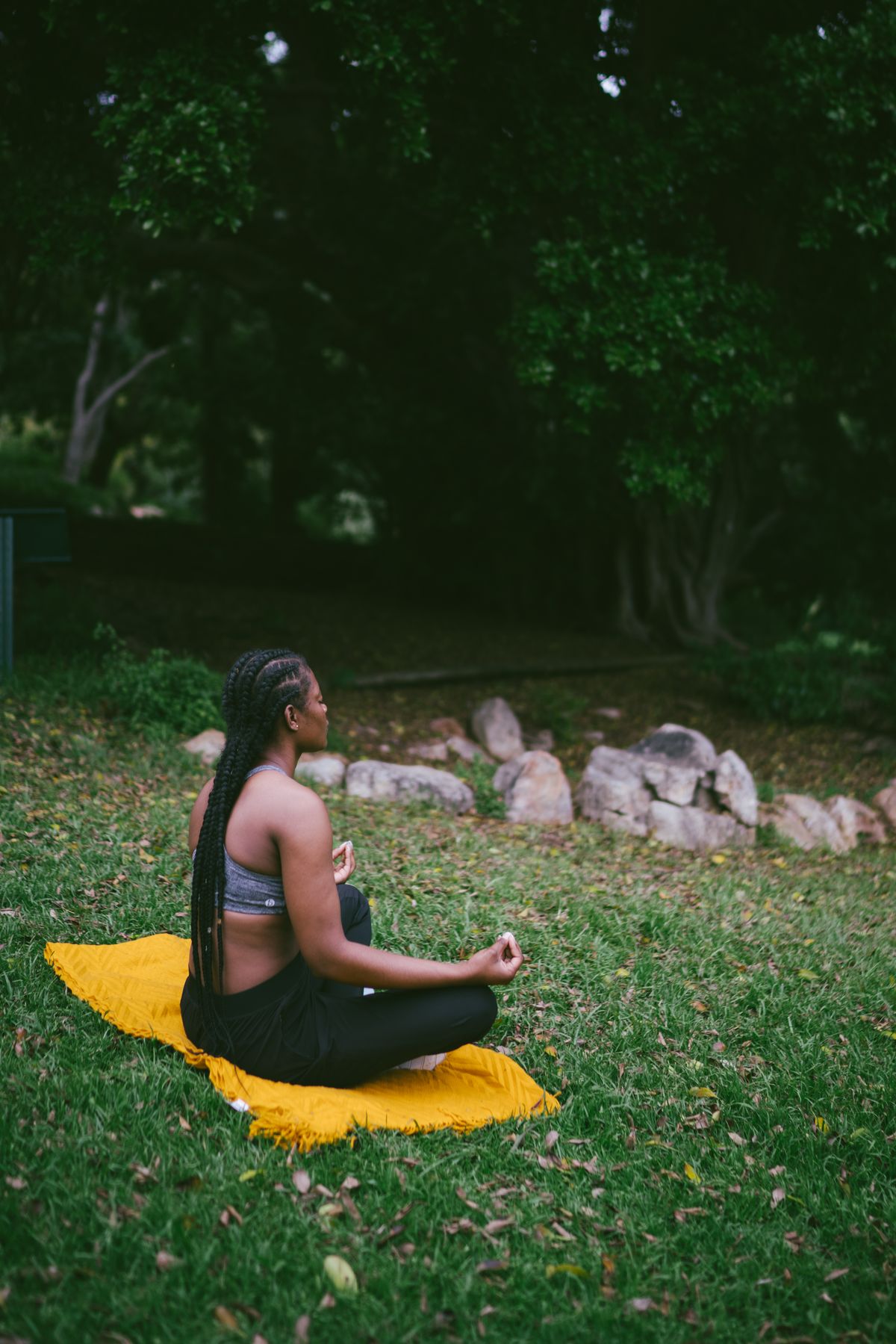 Mujer meditando de perfil sobre una manta amarilla en un parque, con las manos en mudra