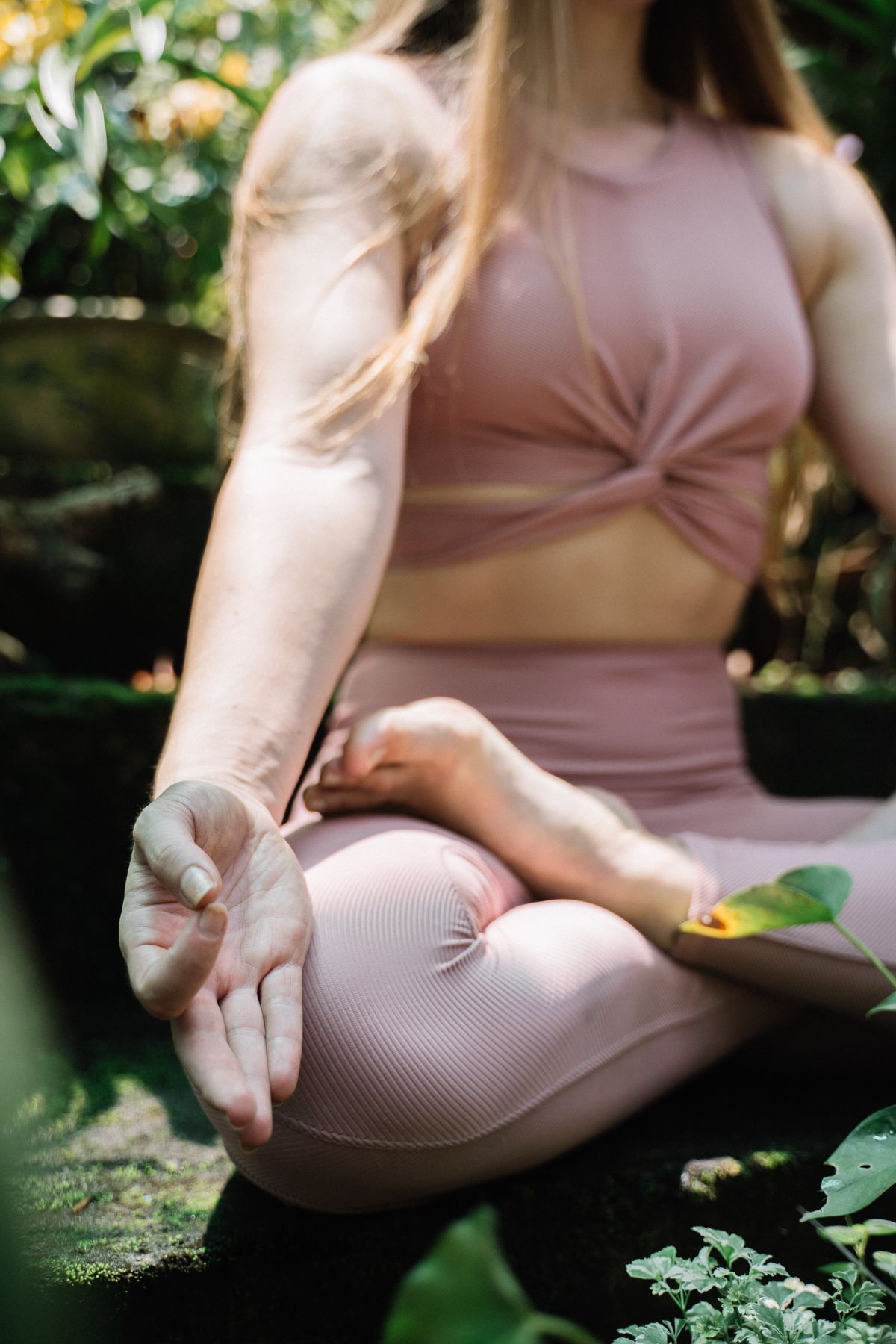 Mujer sentada con las piernas cruzadas en un jardín tropical practicando un mudra con la mano