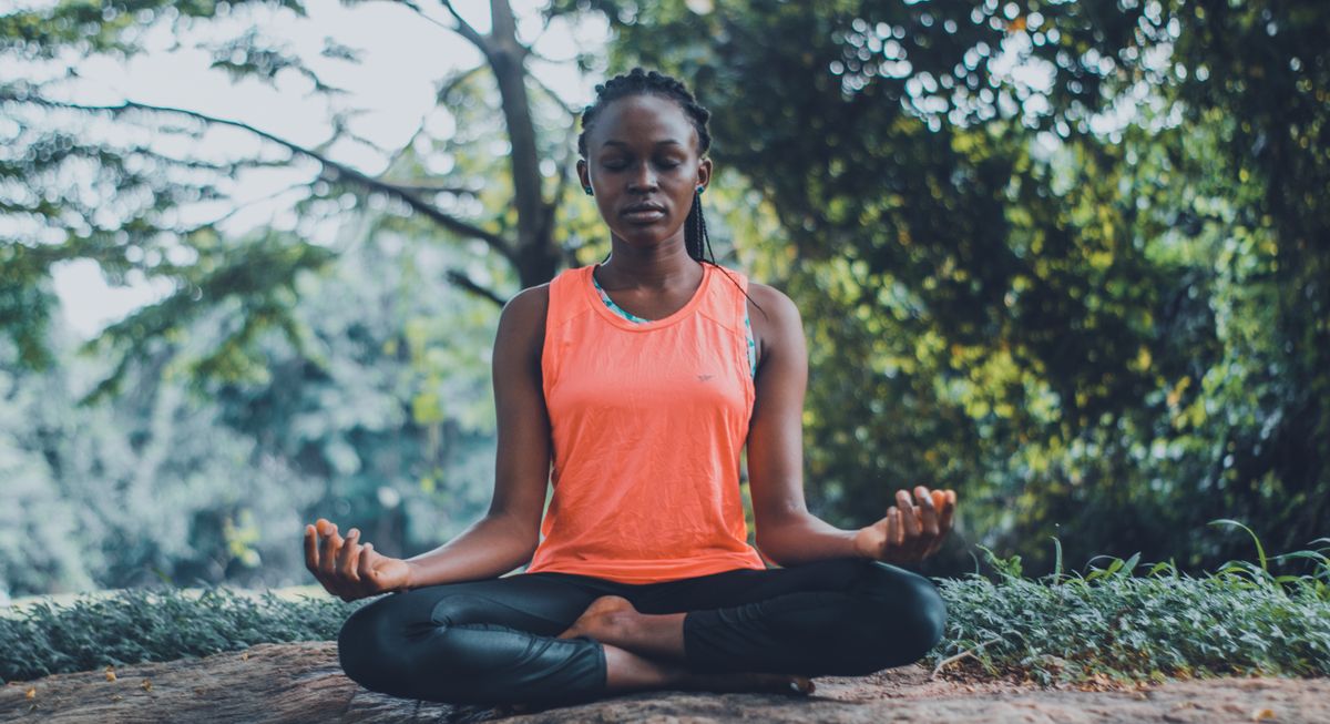 Mujer meditando sentada en flor de loto al aire libre con las manos en gyan mudra sobre las rodillas