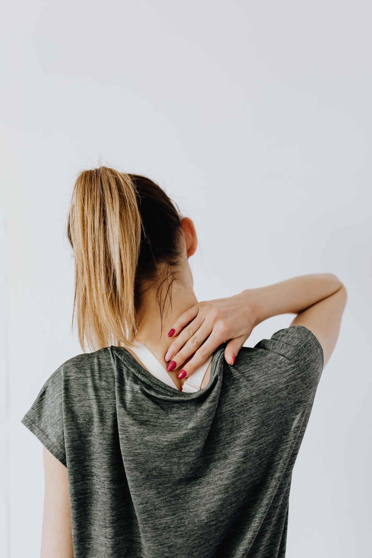 Yoga en la oficina: 10 ejercicios que puedes hacer en tu silla Mujer de espaldas llevándose la mano a la nuca por tensión cervical